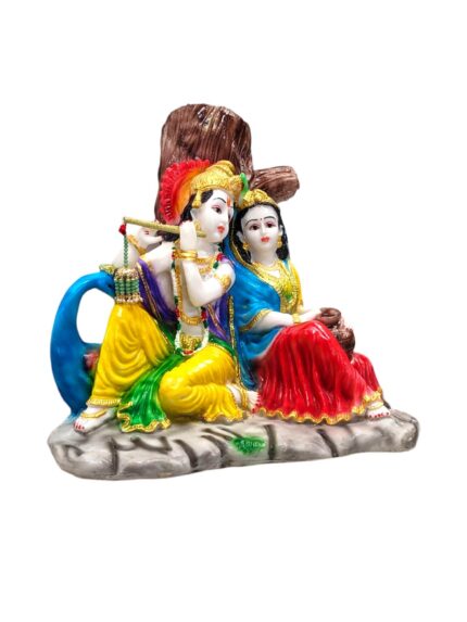 Side view of Radha Krishna Idol sitting besides each other in front of a tree listening to the blissful tones of Krishna flute