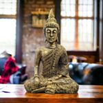 Image of a golden oxidized meditating Buddha statue placed on a wooden platform in a living room setting