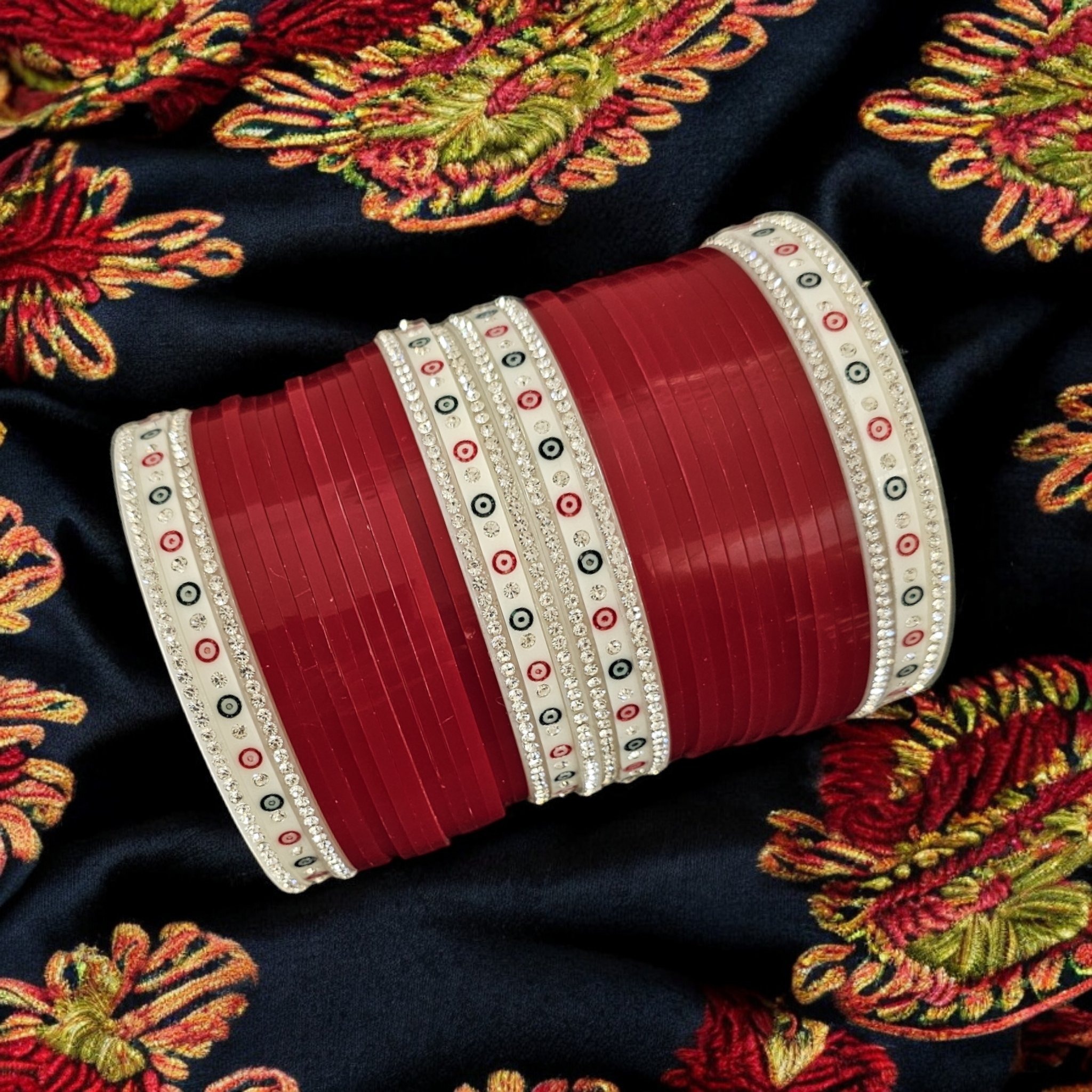 Blood Red Chura with silver gemstones on a dark embroidered scarf as background.