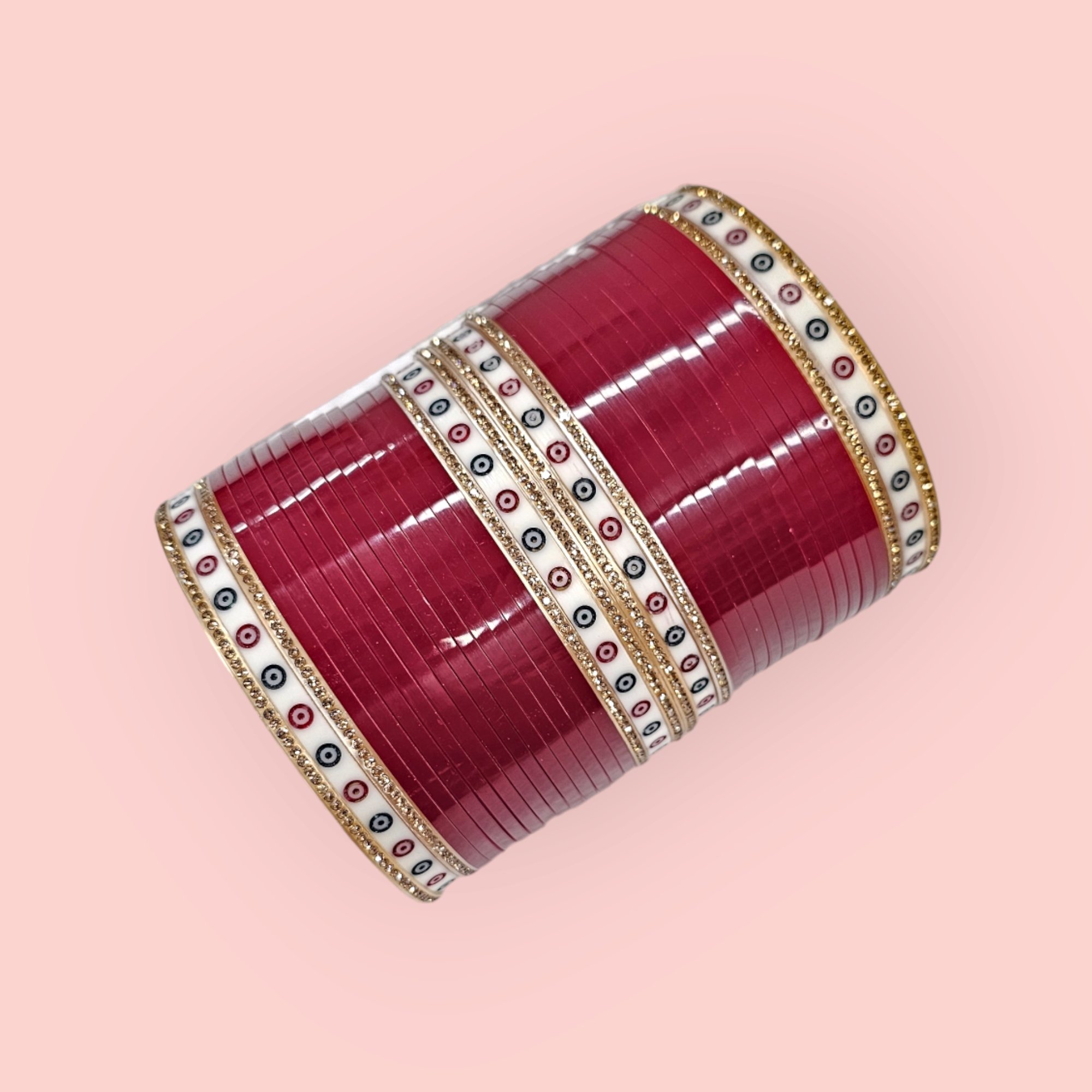 Blood Red Chuda with rose-gold gemstones on a pink background.