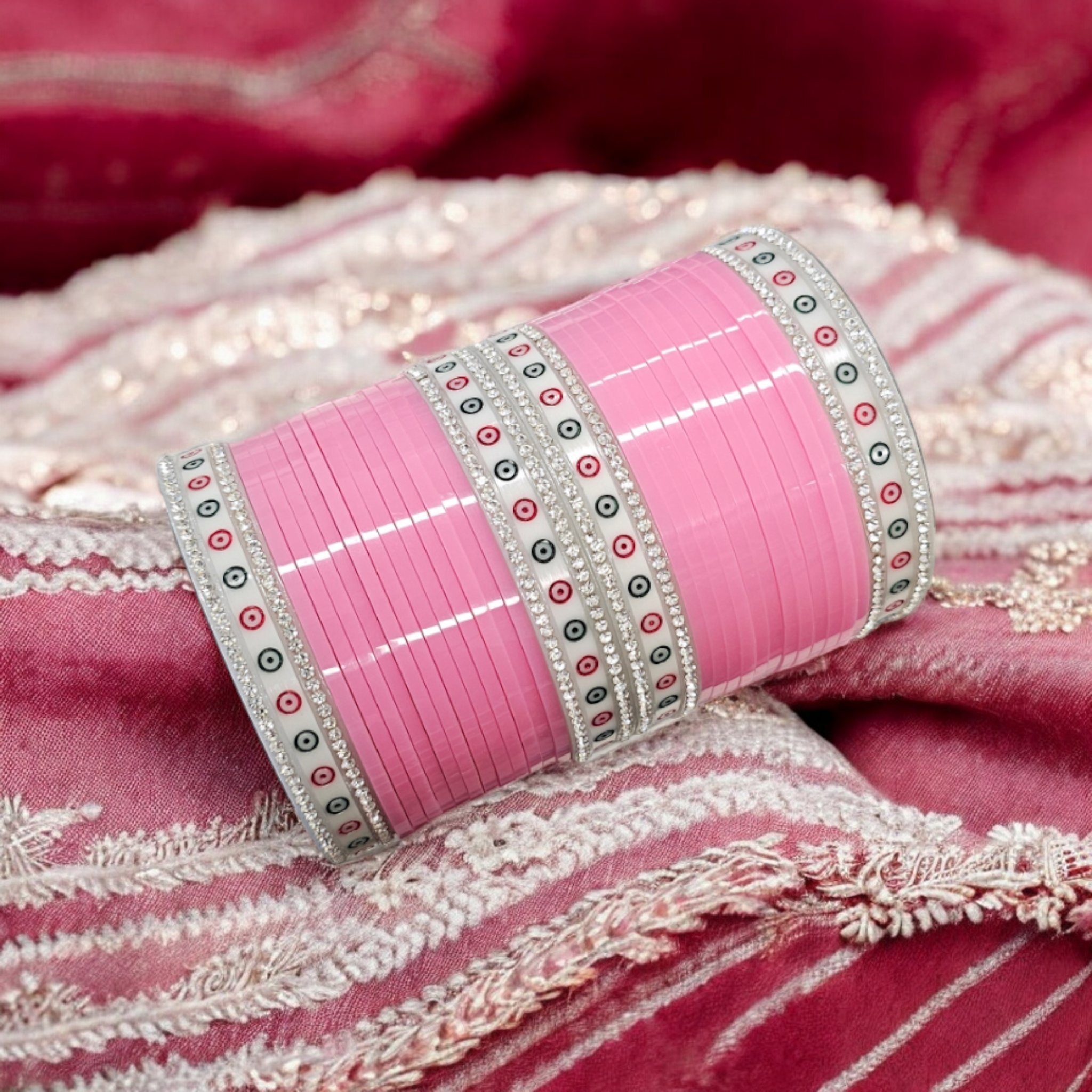 Pink colored Chura with silver gemstones on a pink embroidered background.