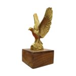 Profile view of a soaring brass eagle statue showcasing its wide wingspan on a wood stand.