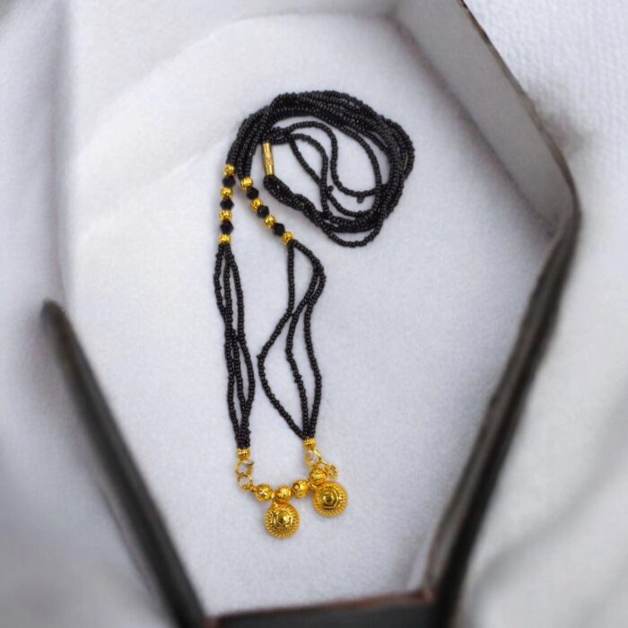 Two Wati Mangalsutra necklace with gold plating and black bead chain, laid flat on a white velvet pad